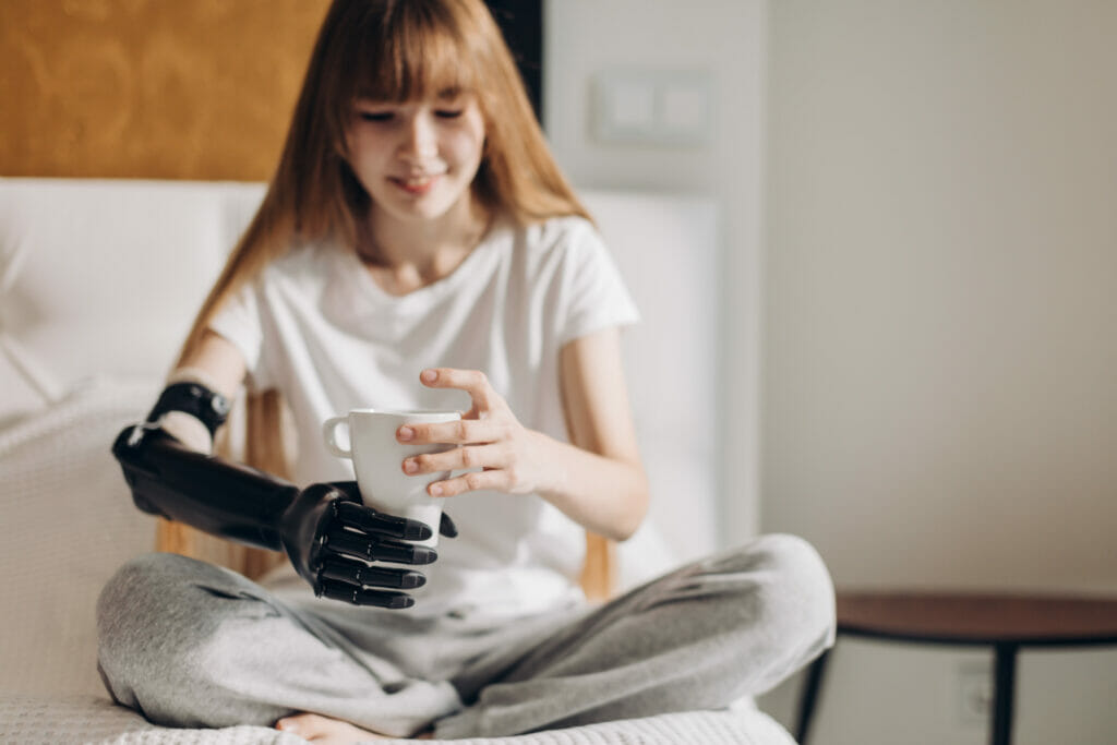 smiling girl with prosthetic cyber arm holding a cup in the room. close up photo.