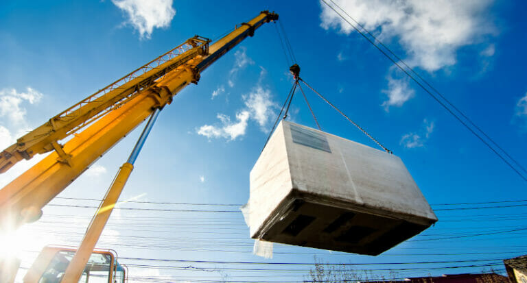 Construction workers using an industrial crane to lift an electric generator