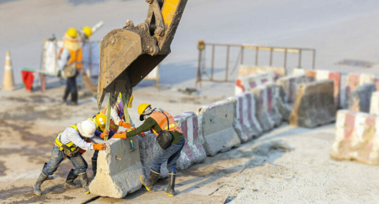 Many workers wear safety suits helped to lift and arrange the cement concrete barriers by excavator In harmony and actively on the road