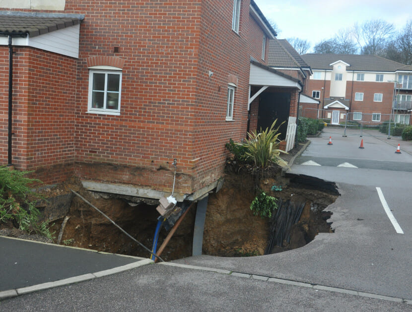 A building with a large sinkhole where the ground and foundation have left the underside of a house exposed
