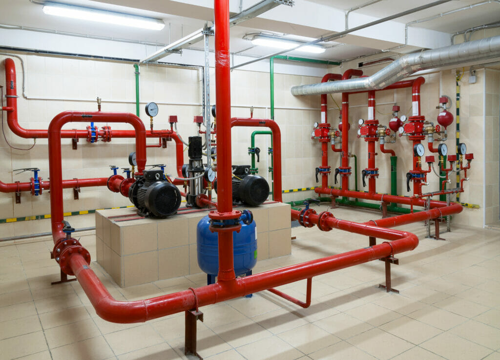 Image of an industrial fire sprinkler station. The pipes are red and lead to a multitude of different avenues to combat fire, connected to an alarm system.